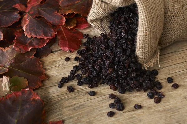 Raisins noirs dans un sac en toile de jute sur une table en bois — Photo