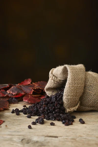 Black raisins in burlap bag over wooden table — Stock Photo, Image