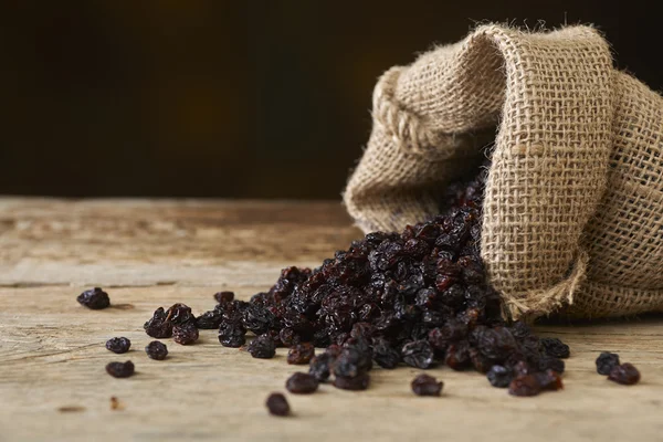 Black raisins in burlap bag over wooden table — Stock Photo, Image