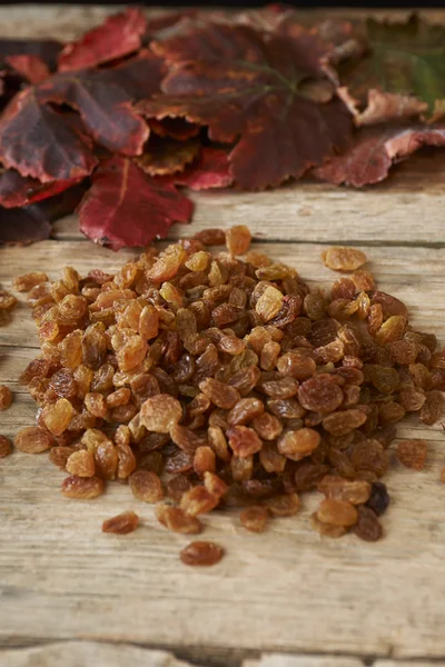 Pasas doradas sobre mesa de madera con hojas de uva de otoño — Foto de Stock