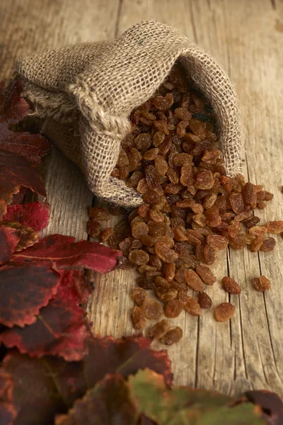 Golden raisins in burlap bag over wooden table — Stock Photo, Image