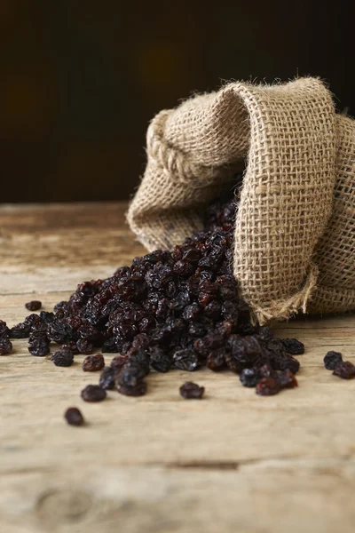 Black raisins in burlap bag over wooden table — Stock Photo, Image