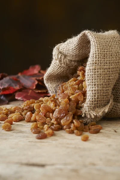 Golden raisins in burlap bag over wooden table — Stock Photo, Image