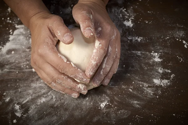 woman's hands kneading dough on wooden table