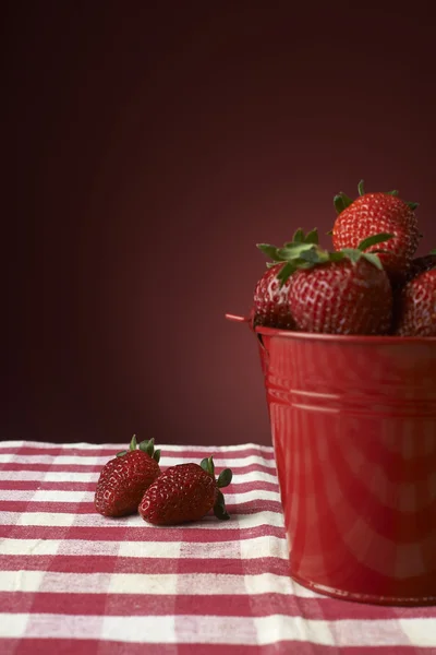 fresh red strawberries in a red bowl on checkered tablecloth