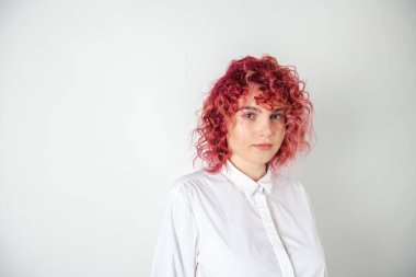 Güzel kızıl saçlı kız beyaz bir arka planda poz veriyor. Yüzünde duygular var.