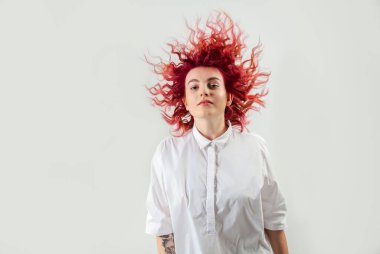 Güzel kızıl saçlı kız beyaz bir arka planda poz veriyor. Yüzünde duygular var.