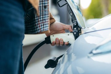 Elektrikli araç şarj istasyonunda güç kaynağı kablosu tutan adam. Yakın plan.