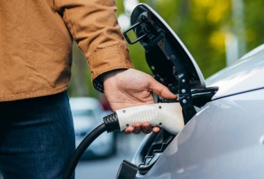 Elektrikli araç şarj istasyonunda güç kaynağı kablosu tutan adam. Yakın plan.