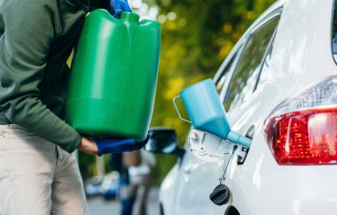 Genç adam, plastik yeşil bir kutudan boş bir yakıt deposuna benzin döküyor. Kapat.