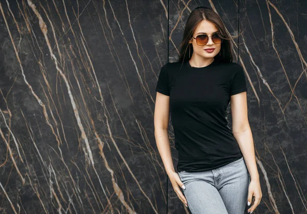 Siyah tişörtlü, güneş gözlüklü şık esmer kız sokakta poz veriyor, kentsel giyim tarzı. Sokak fotoğrafı.