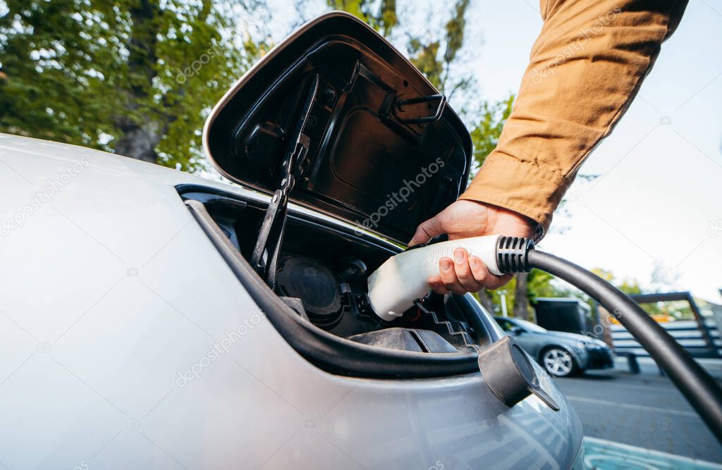 Man holding power supply cable at electric vehicle charging station. Close-up