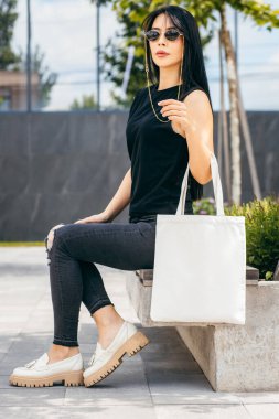 Sokaktaki genç Asyalı manken kız elinde beyaz bir çanta tutuyor.