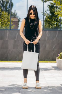 Sokaktaki genç Asyalı manken kız elinde beyaz bir çanta tutuyor.