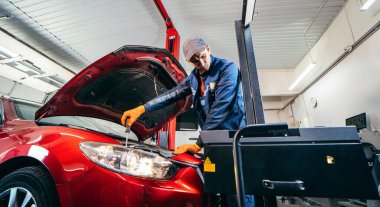 Araba servisindeki kırmızı modern arabanın farlarını ayarlayan genç bir tamirci.