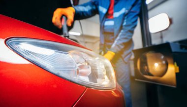 Araba servisindeki kırmızı modern arabanın farlarını ayarlayan genç bir tamirci.