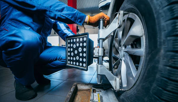 Auto mechanic installing sensor during suspension adjustment and automobile wheel alignment work at repair service station. Close up