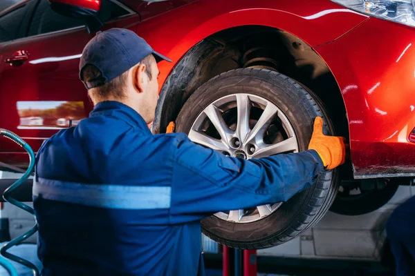 Expert specialist technician changes tires, tyres of lifted up car at auto service, wears uniform costume.