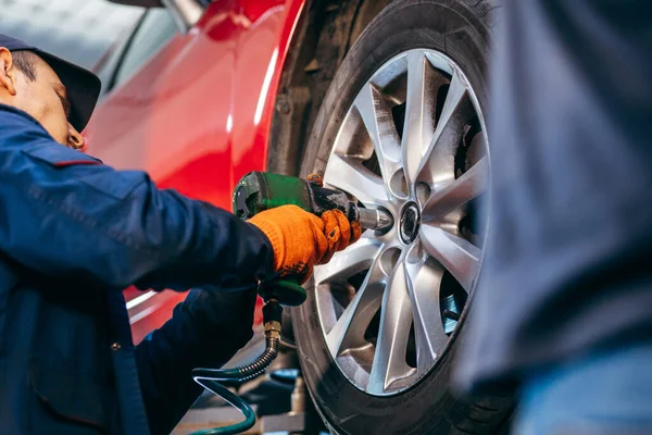 Hands of mechanic with tool, changing tyre of car at auto service