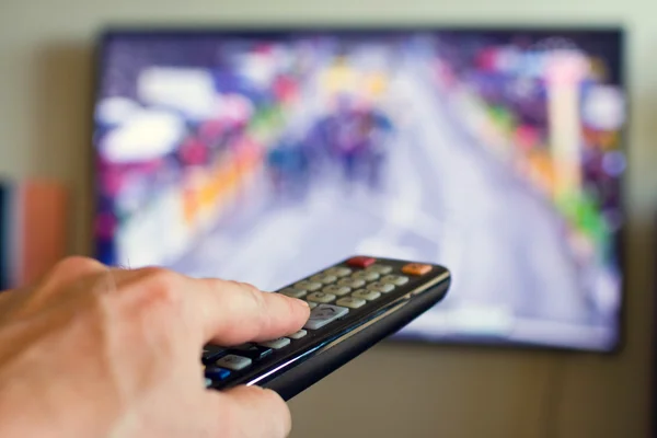 Hand holding TV remote control with a television in the background. — Stock Photo, Image