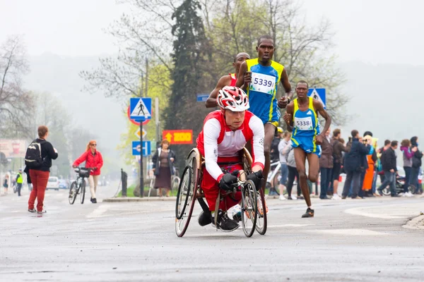 KRAKOW, POLAND - APRIL 28 : Cracovia Marathon.Handicapped man marathon runners in a wheelchair and other runners on the city streets on April 28, 2013 in Krakow, POLAND — Stock Photo, Image