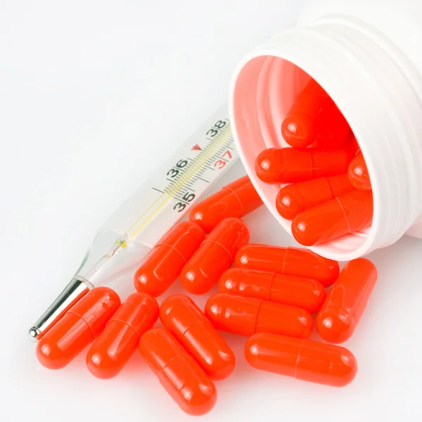Pillole arancioni e termometro su sfondo bianco — Foto Stock