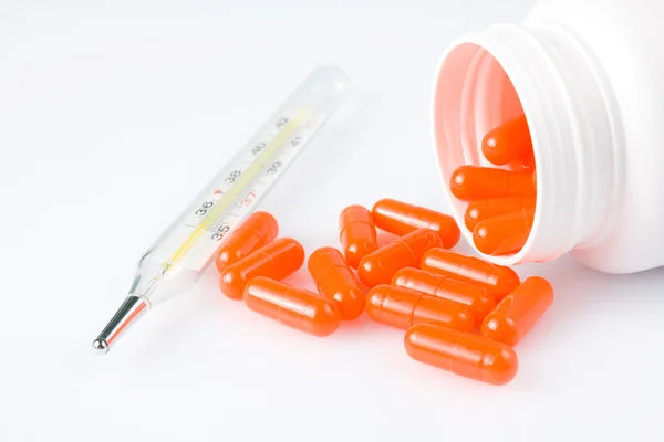 Comprimidos laranja e termômetro no fundo branco — Fotografia de Stock
