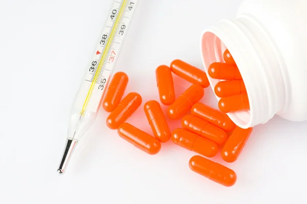 Pilules orange et thermomètre sur fond blanc — Photo