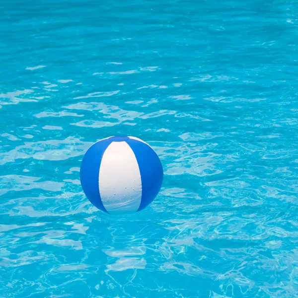 Vita och blå badboll som flyter på en gnistrande blå pool — Stockfoto