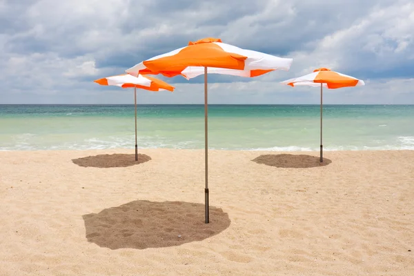 Bulutlu mavi gökyüzü ve güneş ile beyaz kum plajı üzerinde plaj şemsiyeleri — Stok fotoğraf