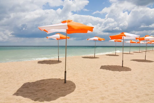 Beach umbrellas on the white sand beach with cloudy blue sky and sun — Stock Photo, Image