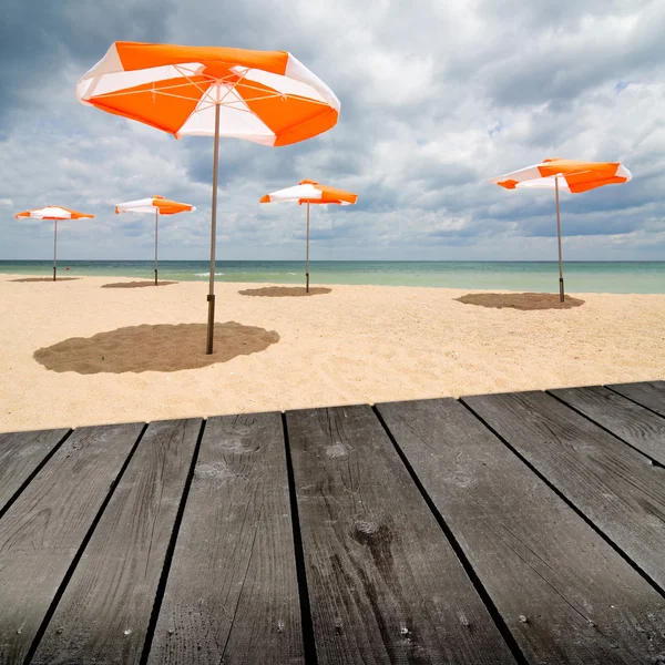 Guarda-chuvas de praia na areia branca e mesa de deck de madeira vazia . — Fotografia de Stock