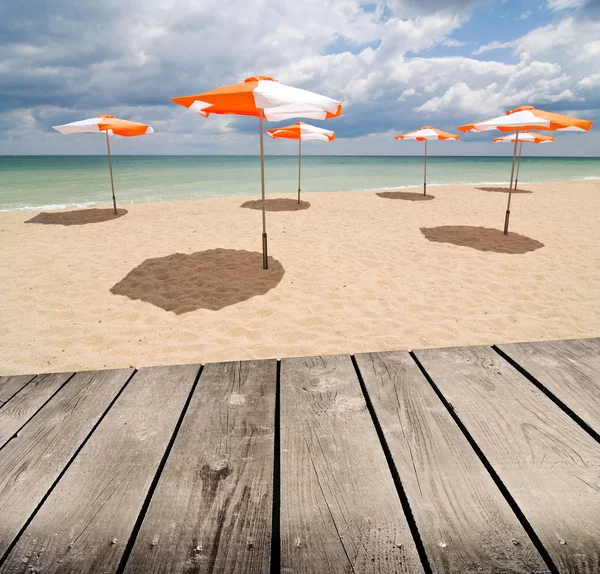 Sonnenschirme am Strand und leerer Holzdecktisch. — Stockfoto