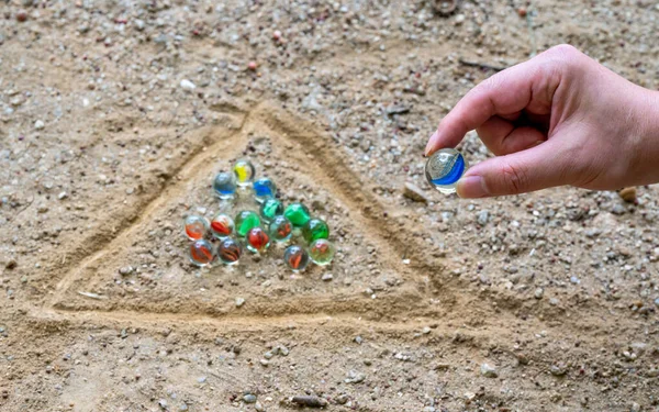 The hand of a man playing marbles in a playground with dirt — Stock Photo, Image