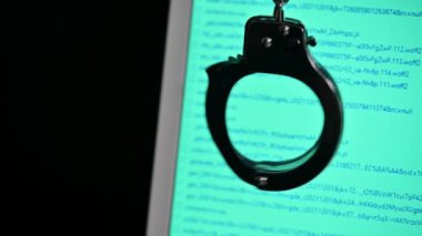 Görünür program kodlu bulanık bilgisayar ekranı ve kelepçeler. Siber suç kavramı