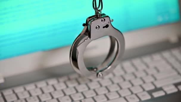 Blurred computer screen with program code visible, and shaking handcuffs. Cybercrime concept — Stock Video