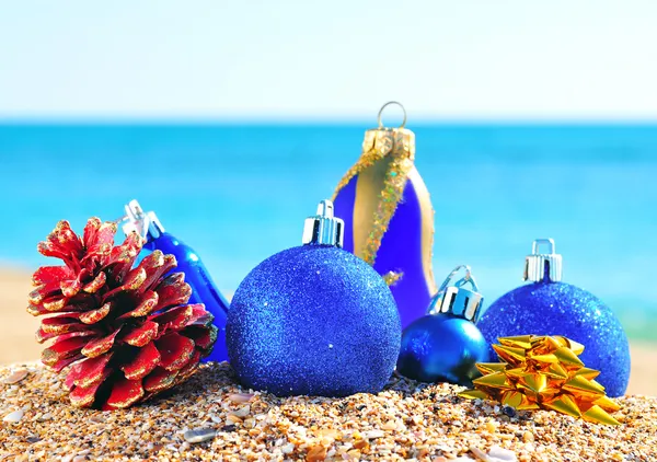 Blauwe kerstballen en kegels op het zand in de kust — Stockfoto