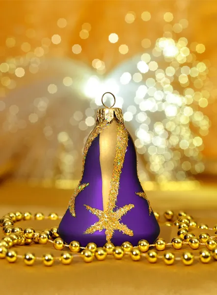 Campana púrpura de Navidad con cuentas alrededor en backgrou luz dorada —  Fotos de Stock