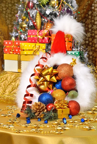Weihnachtsmütze mit Geschenkschachteln, Christbaumkugeln auf Christbaumbackgr — Stockfoto