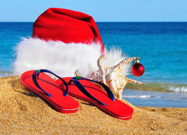 Kerstman hoed en slippers aan de kust tegen blauwe hemel — Stockfoto