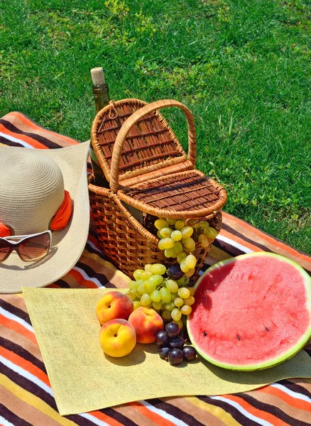 Beach hat, sun glasses, picnic basket with fruits and bottle of — Stock Photo, Image