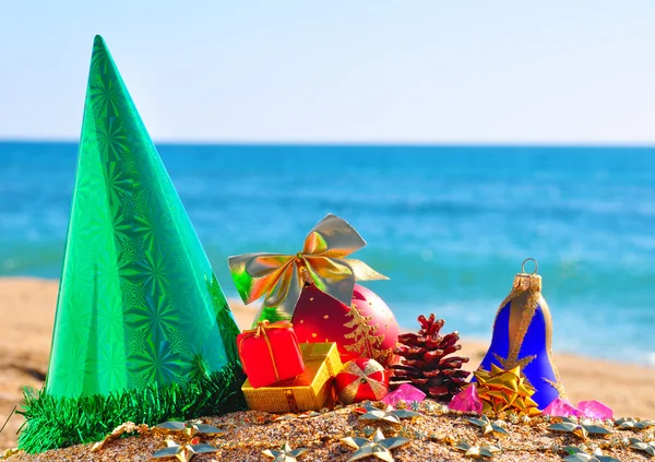 Kerstballen, doos van de gift en kegel op het zand in de kust — Stockfoto