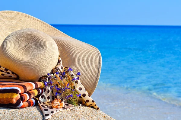 Woman beach hat, bright towel and flowers against blue ocean — Stock Photo, Image