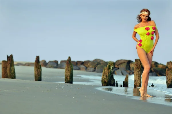 Mode-Modell in maßgeschneiderter Limettenfarbe Badebekleidung mit Blumen, die am Strand bei Sonnenuntergang posiert — Stockfoto