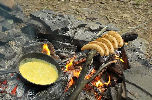 Spiegeleier am Feuer in eiserner Pfanne mit Grillwürsten am Spieß — Stockfoto