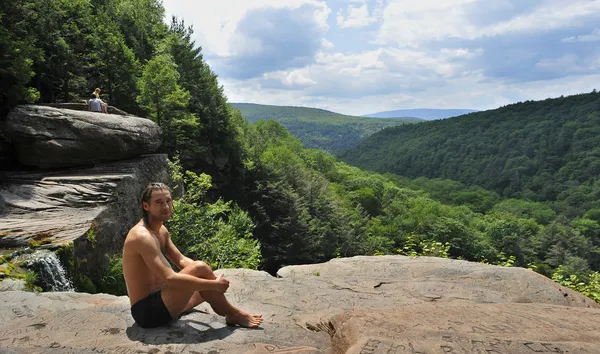 Un turista masculino se encuentra en una cresta de roca con vistas a una parte del panorama. Vista desde la cornisa en la parte superior de la cascada Kaaterskills en las montañas Catskills de Nueva York — Foto de Stock