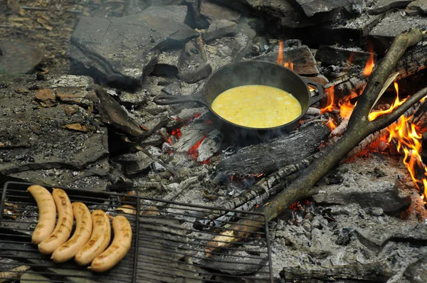 Spiegeleier in eiserner Pfanne mit Grillwürsten in Flammen — Stockfoto