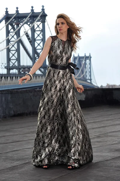 Modelo de moda posando sexy, vestindo vestido de noite longa no telhado localização com construção de ponte de metal no fundo — Fotografia de Stock