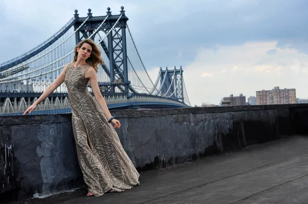Modelo de moda posando sexy, usando vestido de noche largo en la ubicación de la azotea con la construcción de puente de metal en el fondo —  Fotos de Stock