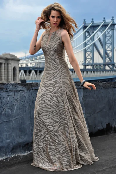 Modelo de moda posando sexy, vestindo vestido de noite longa no telhado localização com construção de ponte de metal no fundo — Fotografia de Stock